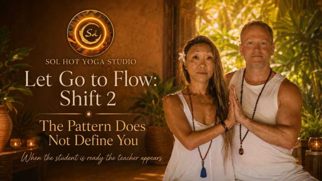 Two people in white outfits with hands pressed together in a prayer pose, standing beside a warm Sol Hot Yoga Studio banner that reads "Let Go to Flow: Shift 2".