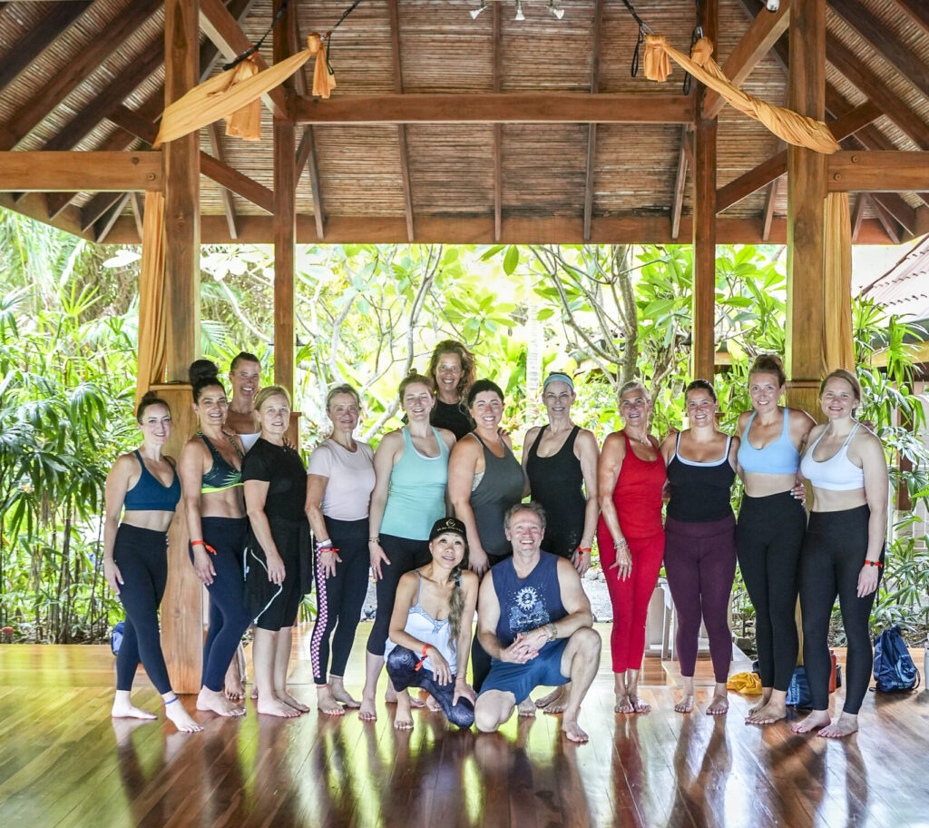 retreat thank you Sol Hot Yoga Studio Group of fitness participants in colorful athletic wear posing for a photo inside a tropical wooden pavilion with plants outside.