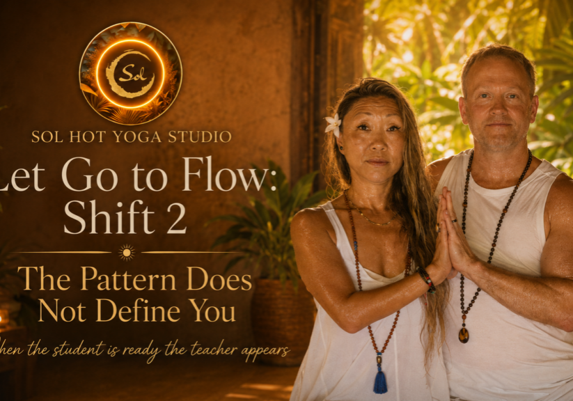 Two people in white outfits with hands pressed together in a prayer pose, standing beside a warm Sol Hot Yoga Studio banner that reads "Let Go to Flow: Shift 2".
